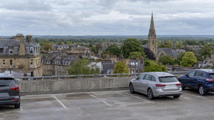 Cars on the top deck of a multi-storey car park looking over the sandstone terraces, slate roofs and a church spire of Harrogate